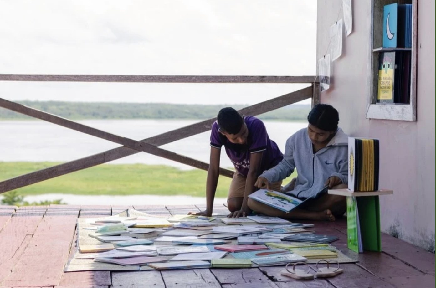 Dois jovens leitores espalhando livros no assoalho da biblioteca comunitária de Uarini